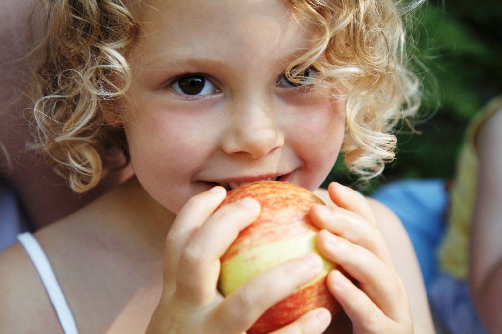女孩(3-5岁)拿着苹果对着嘴，微笑，肖像，特写