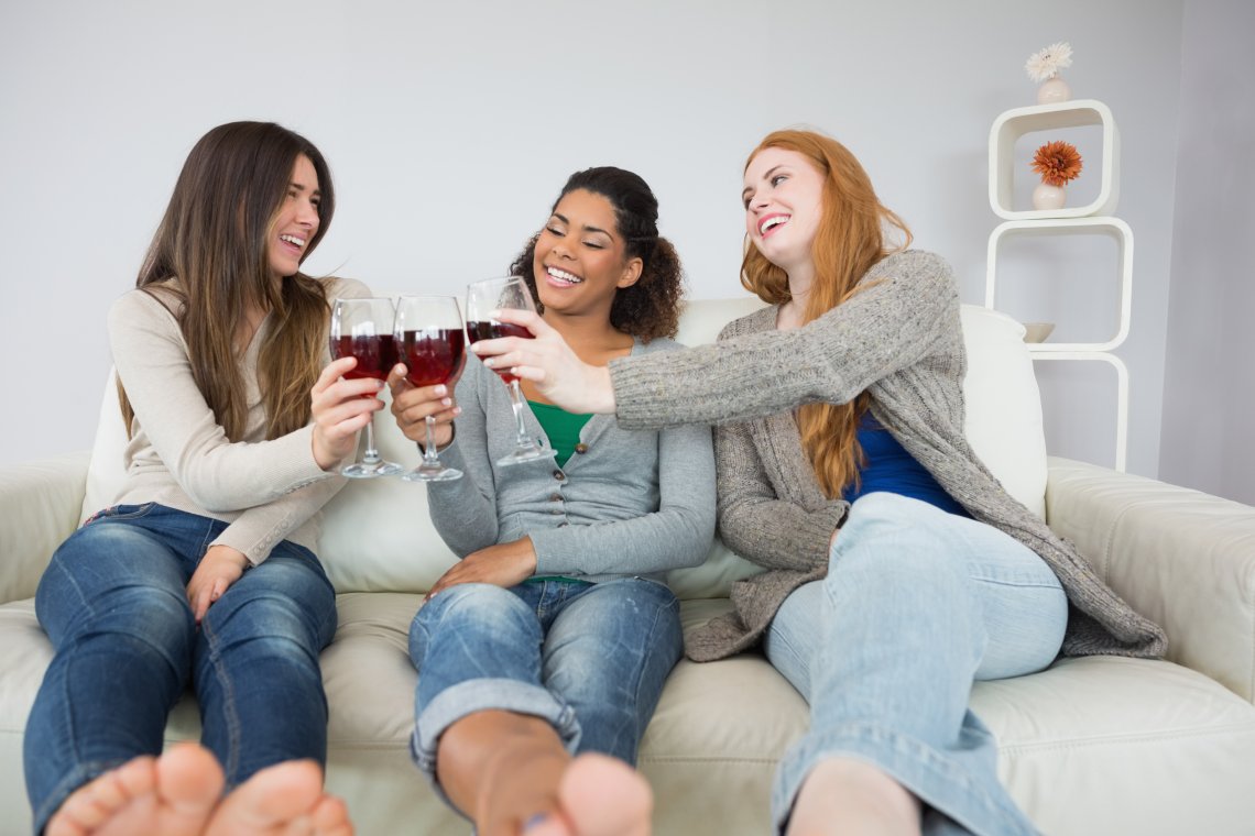 欢快的年轻女性朋友在家里的沙发上举杯敬酒